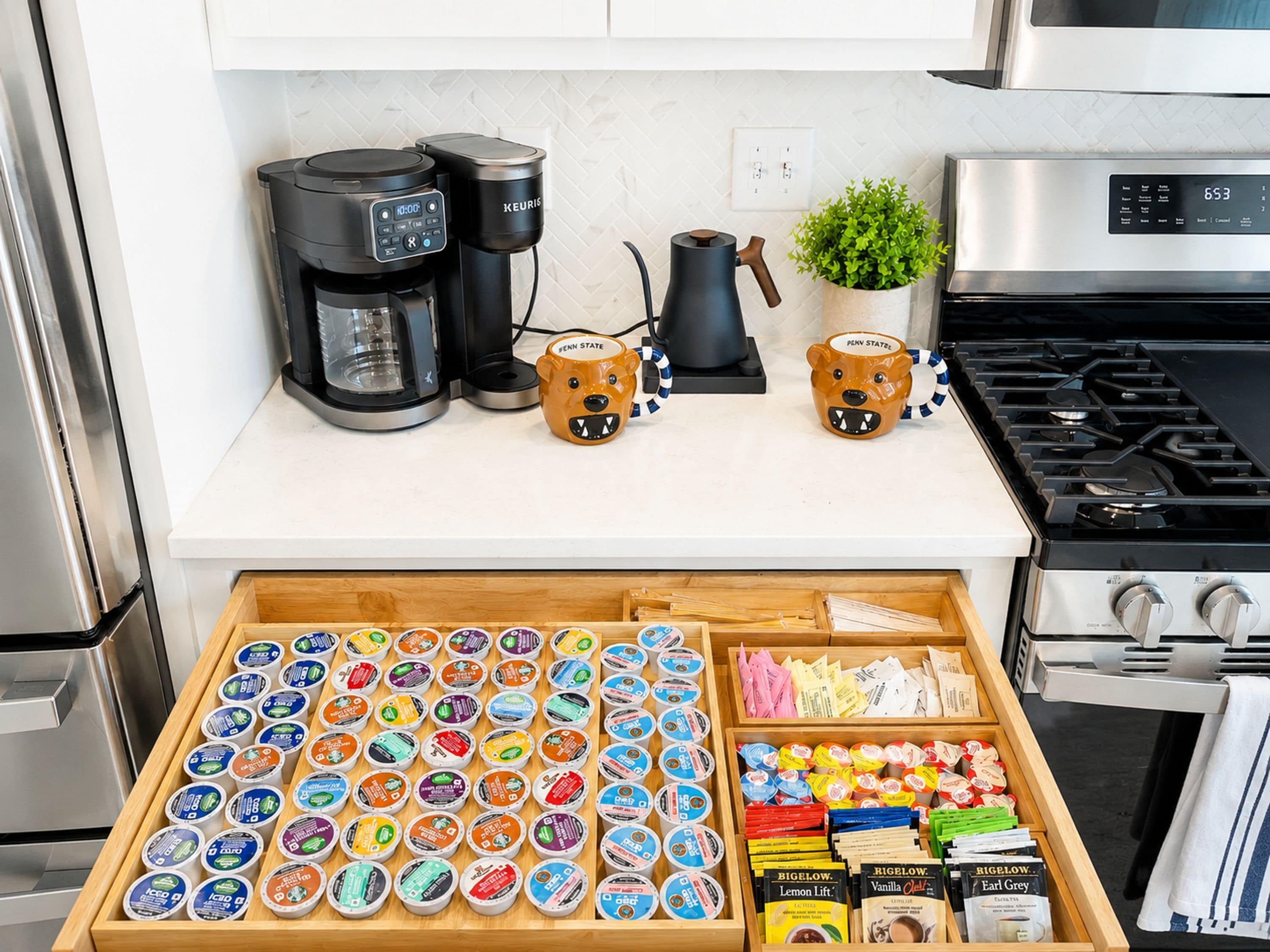 A kitchen with a coffee maker, a kettle, and a stove. Below, there is a drawer with various food items and containers.