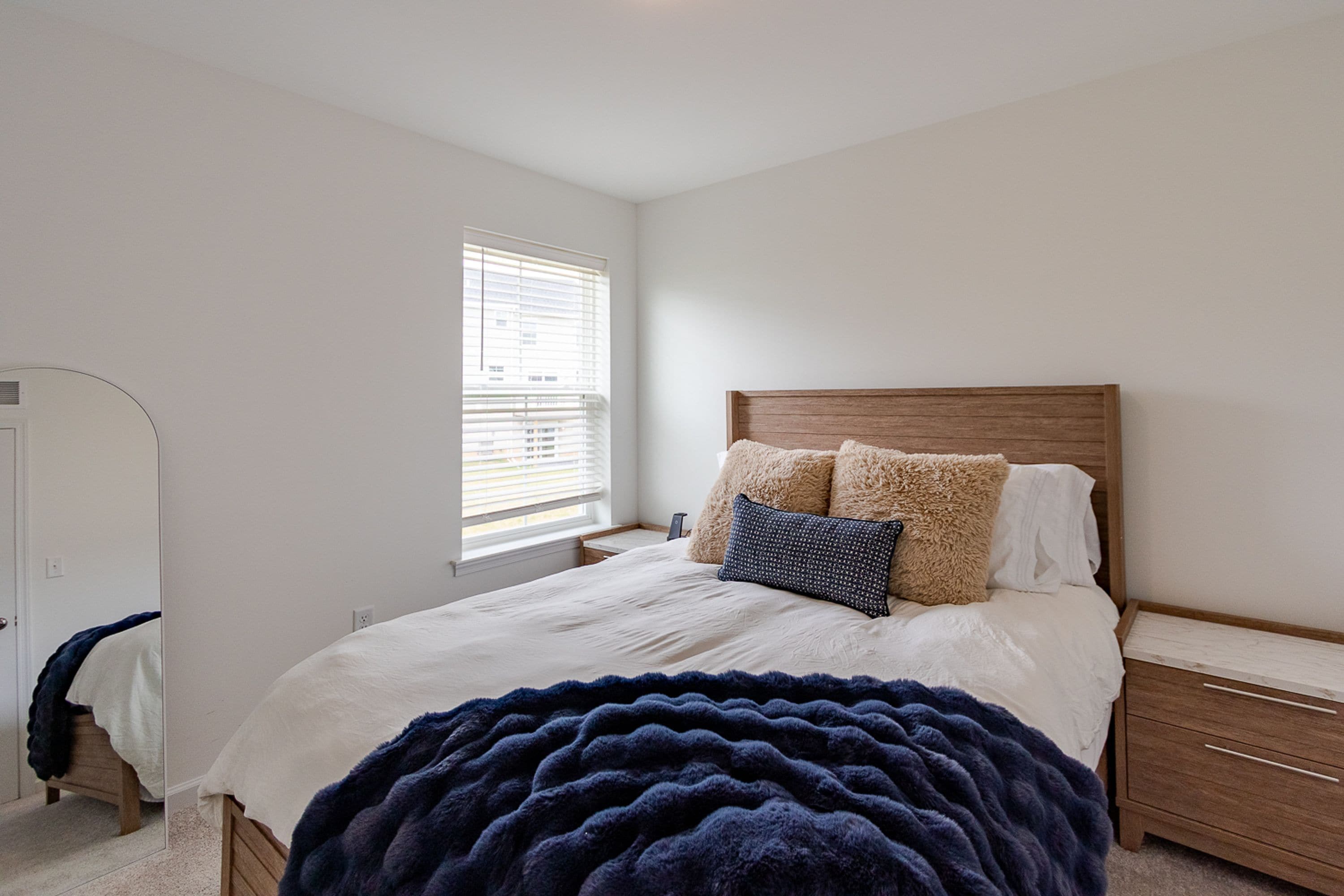 A bedroom with a bed, bedside tables, a window with blinds, a wardrobe, and a blanket.