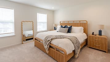 A bedroom with a wooden bed, bedside tables, a mirror, and a window with blinds.