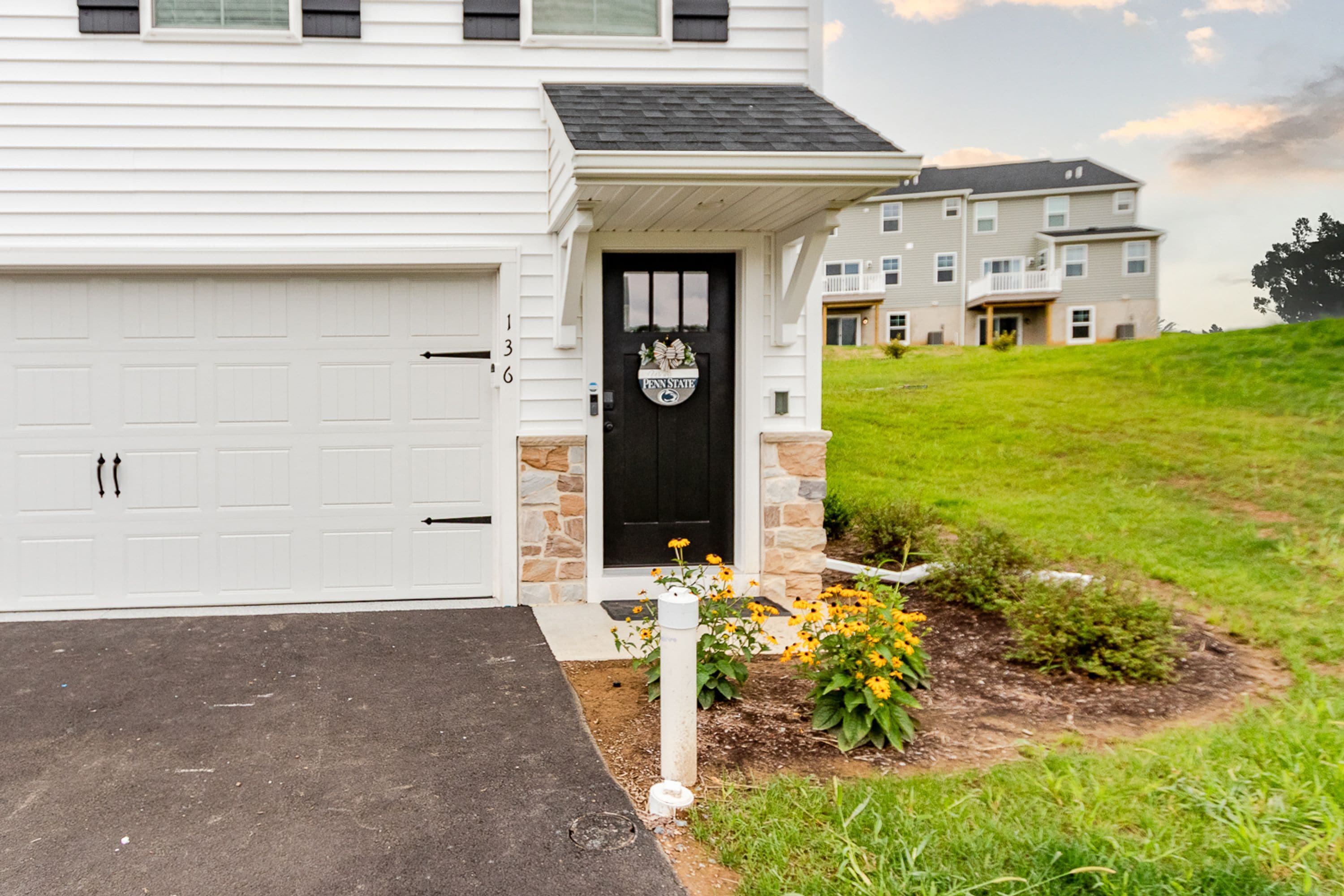A residential house with a white garage door, a black front door with a Penn State logo, and a stone porch.