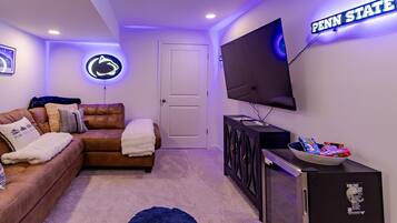 A living room with a large flat-screen TV mounted on the wall, a leather sofa, a small cabinet, and a neon sign.