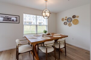 Un comedor con mesa de madera, sillas blancas y una lámpara colgante.
