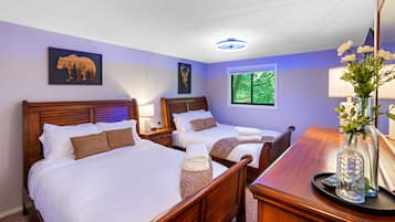 Ein Hotelzimmer mit zwei Betten, einem Nachttisch, einem Schreibtisch, einer Lampe und einem Fenster mit Blick auf Grünflächen.