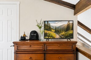 Une commode en bois sur laquelle est posée une télévision, et qui diffuse une image d’un paysage de montagne.