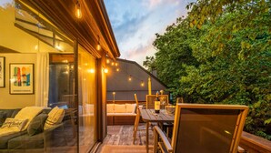 A modern outdoor seating area with a wooden table and chairs, a cushioned bench, and a glass wall overlooking a garden. - Camelback Home Family Friendly Waterpark Arcade (Tannersville)
