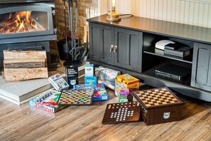 Un salon chaleureux avec une cheminée, un meuble contenant des appareils électroniques et divers jeux de société disposés sur le sol.
