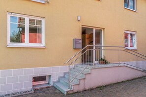 A building with a pink exterior, a set of stairs leading to a landing, and a small window with a curtain.