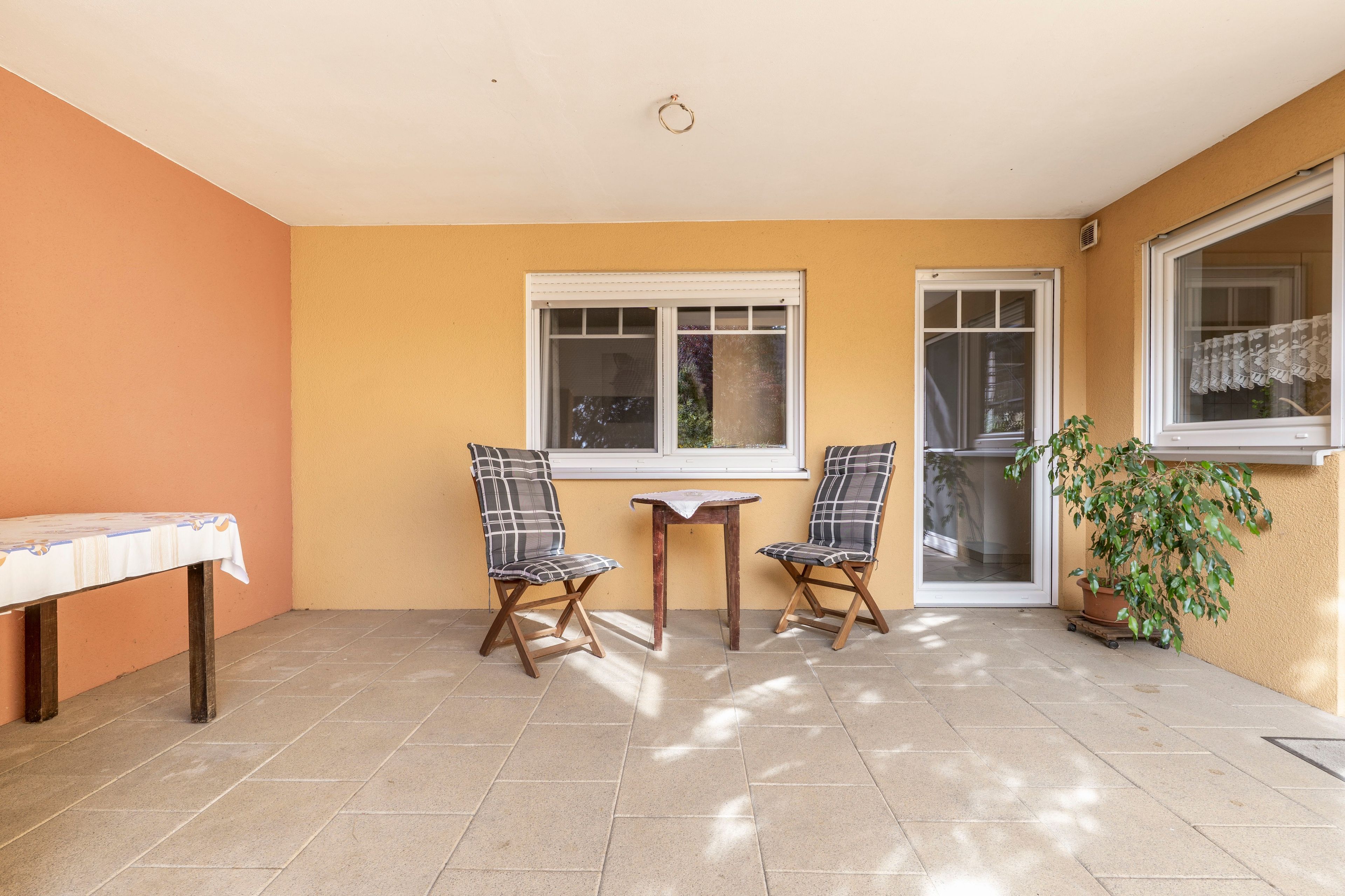 Eine Terrasse mit zwei Stühlen, einem kleinen Tisch und einem Blumentopf.