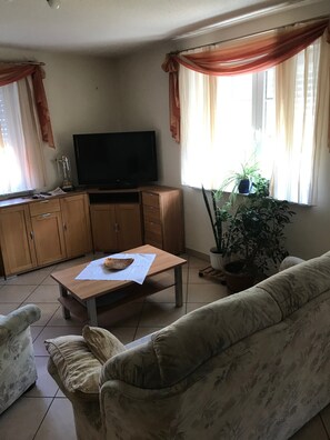 Een woonkamer met een televisie, houten kasten, een bank, een salontafel en een potplant.