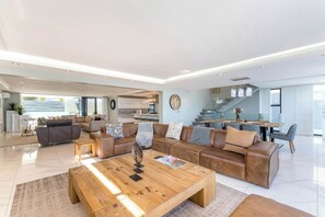 A spacious living area with a large sofa set, a coffee table, and a dining area with a staircase leading to an upper level. - The Blouberg Lookout (Cape Town)