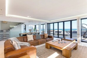 Uma sala de estar moderna com uma janela grande, um conjunto de sofá, uma mesa de centro de madeira e uma escada que leva a um andar superior.