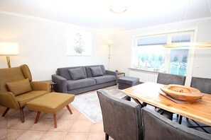 Ein modernes Wohnzimmer mit einer Couch, einem Hocker und einem Esstisch.