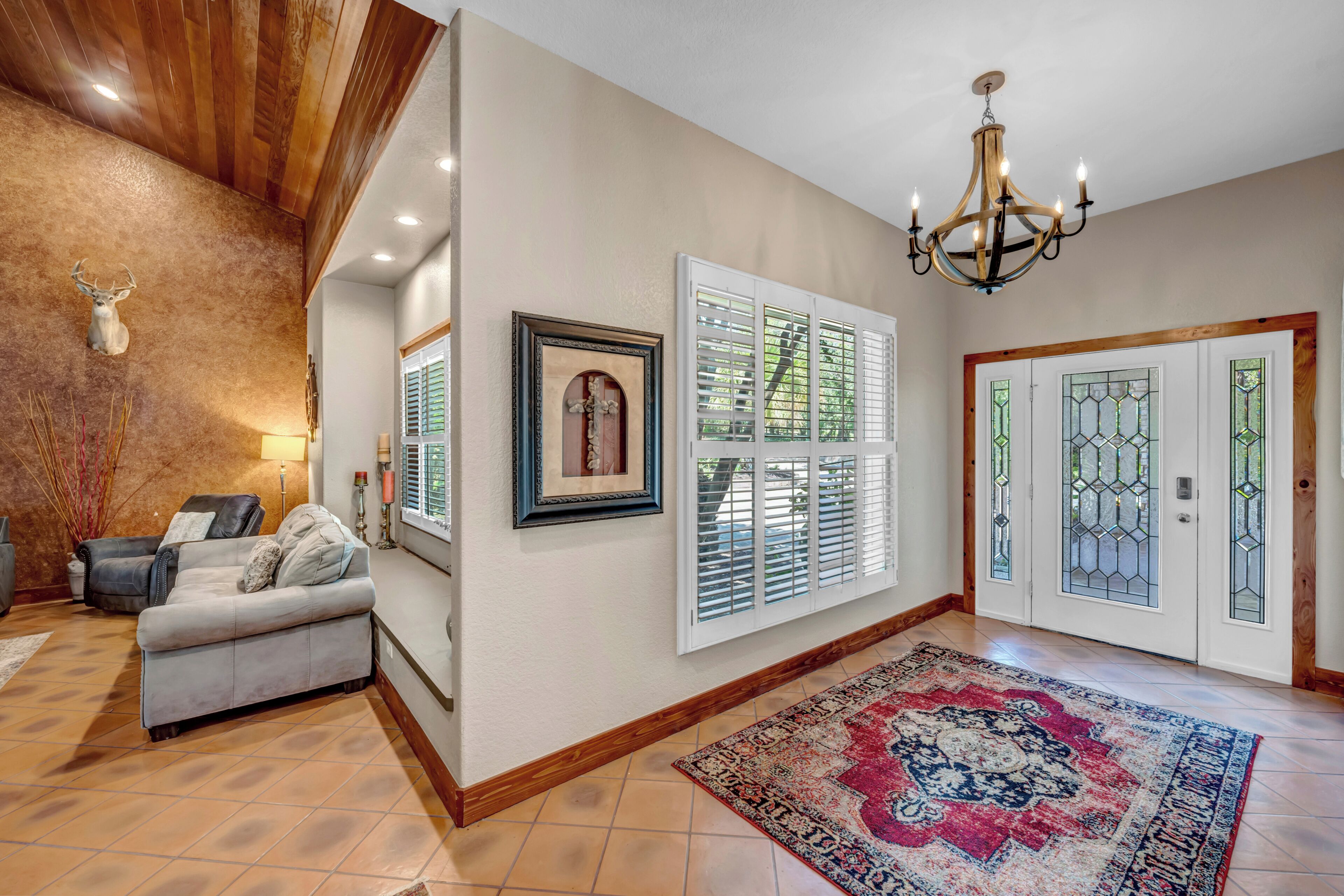 A spacious hallway with a chandelier, a framed picture, and a patterned rug.
