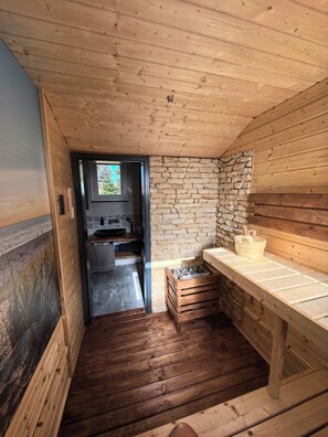 A wooden interior with a stone wall, a wooden bench, and a small kitchen area. - An oasis of peace, where charm and elegance meet nature—a chalet in Western Lusatia (Haselbachtal)