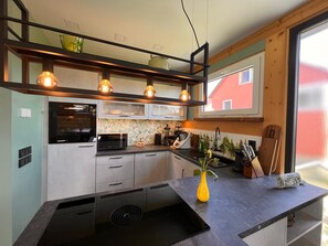 A modern kitchen with a built-in oven, microwave, and a black induction cooktop. - An oasis of peace, where charm and elegance meet nature—a chalet in Western Lusatia (Haselbachtal)