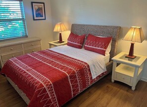 Ein ordentlich bezogenes Bett mit einer rot-weißen Tagesdecke, zwei passende Kissen und zwei Nachttischlampen auf weißen Nachttischen.
