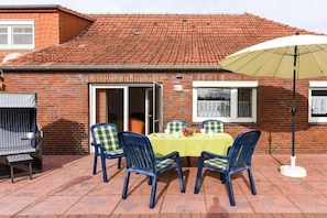 A patio with a table and chairs, a grill, and a brick building with a tiled roof. - Holiday home with 1 bedroom (Bensersiel)