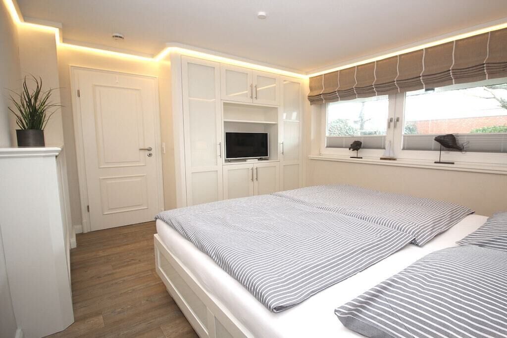 A bedroom with a bed, built-in TV, and a window with blinds.