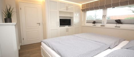 A bedroom with a bed, built-in TV, and a window with blinds.