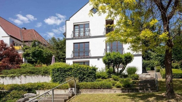 Un edificio a due piani con facciata bianca, un balcone al secondo piano e una scala che conduce all'ingresso.