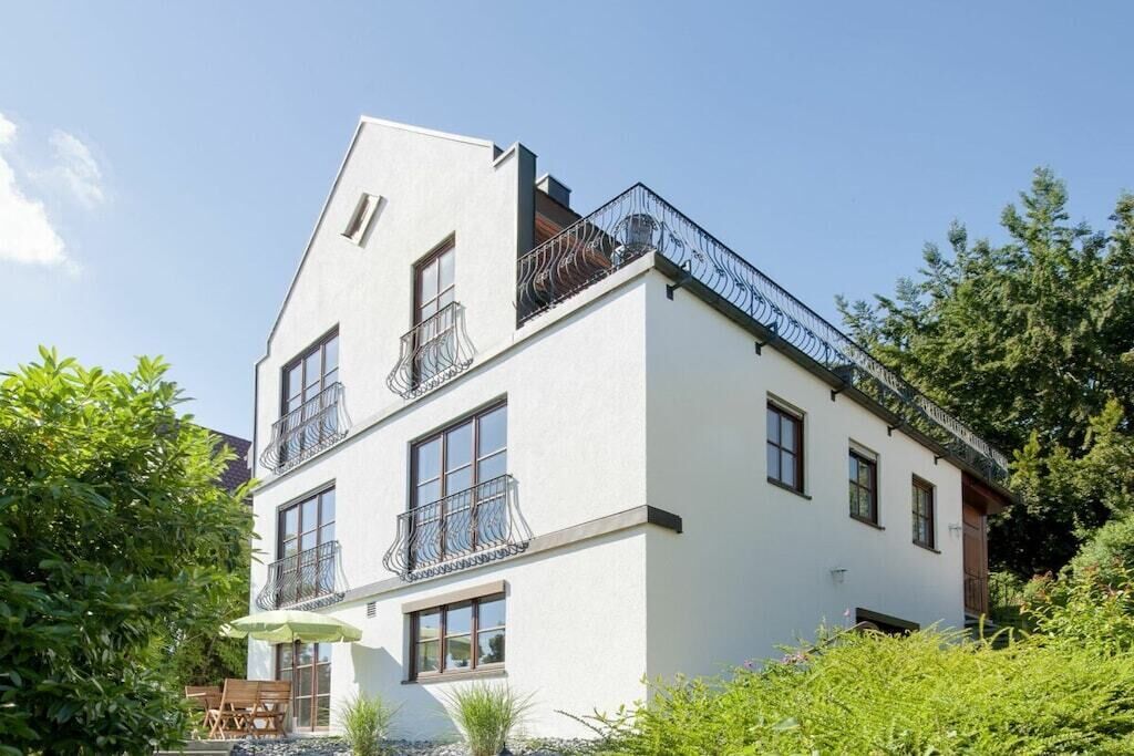 A two-story building with a white facade, multiple balconies, and a small outdoor seating area.