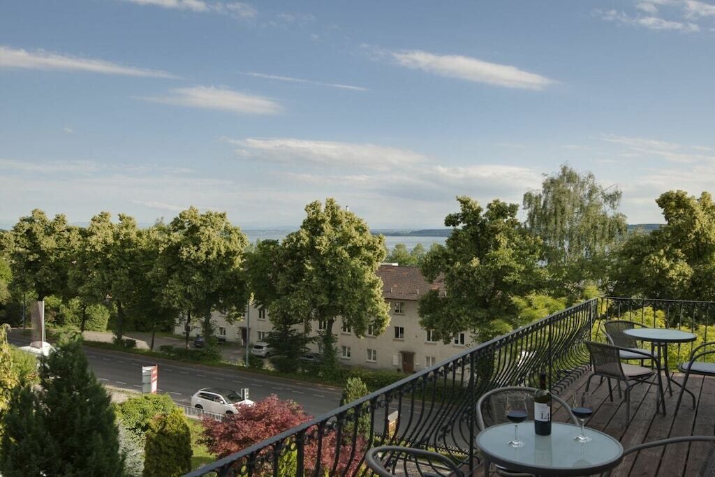 A balcony with outdoor seating, overlooking a street and trees.