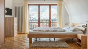 Una camera da letto con un'ampia finestra, un letto, un comodino e un termosifone.