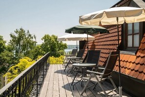 Eine Holzterrasse mit Außenmöbeln und Sonnenschirmen mit Blick auf ein Gewässer.