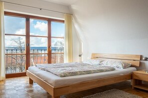 Ein Schlafzimmer mit einem hölzernen Bett, einem Nachttisch und Blick durch große Fenster.