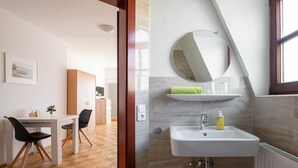 Un bagno moderno con un lavandino bianco, uno specchio rotondo e un portascopevoli.