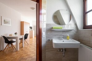Ein modernes Badezimmer mit einem weißen Waschbecken, einem runden Spiegel und einem Handtuchhalter.