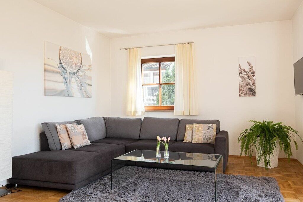 Una sala de estar moderna con un sofá modular, una mesa de centro de vidrio y un ventanal con cortinas.