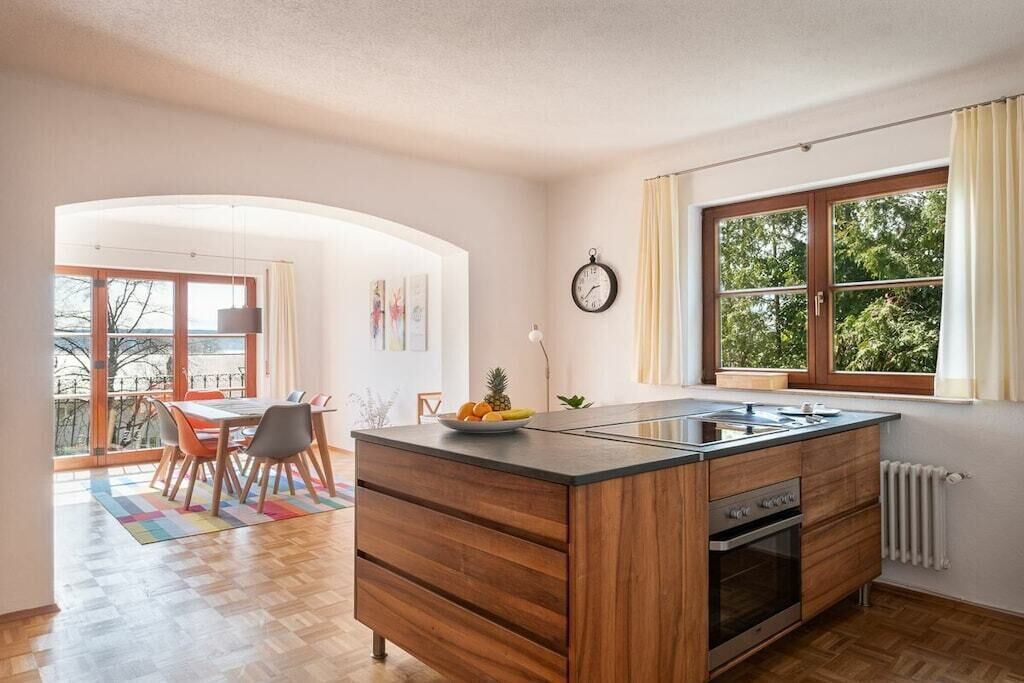 Une cuisine moderne dotée d’un îlot central, de meubles en bois, d’un four encastré et d’une grande fenêtre agrémentée de rideaux.