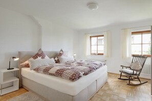 A bedroom with a large bed, bedside tables, a rocking chair, and a window with curtains. - La Perla - Sea Pearl (Überlingen)