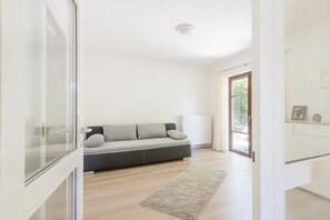 A modern living room with a grey sofa, a white radiator, and a glass door leading to a balcony. - La Perla - Sea Pearl (Überlingen)
