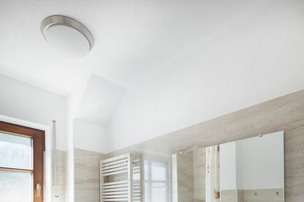 Un baño moderno con un espejo grande, una ducha con puerta de cristal y una lámpara en el techo.