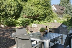 Een terras buiten met een tafel, stoelen, een potplant en een fles wijn.