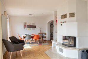 A modern living room with a fireplace, wooden flooring, and a dining area with chairs and a table. - La Perla - Sea Pearl (Überlingen)