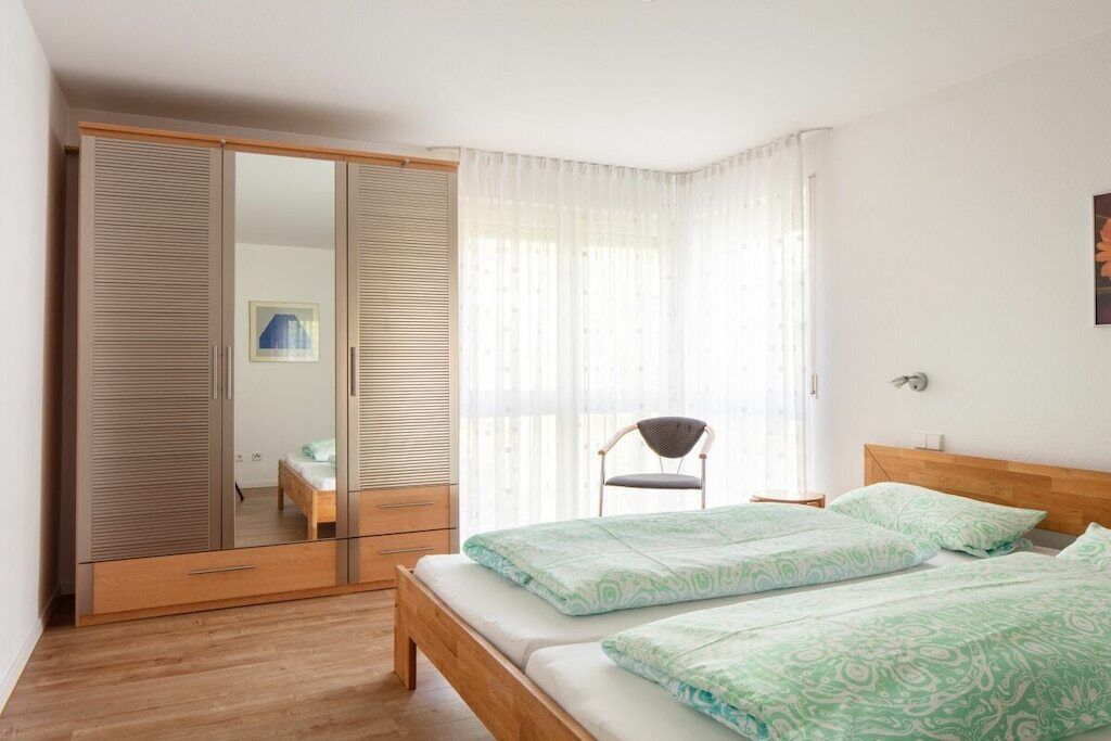 A bedroom with a wooden bed, a mirror wardrobe, and a chair.