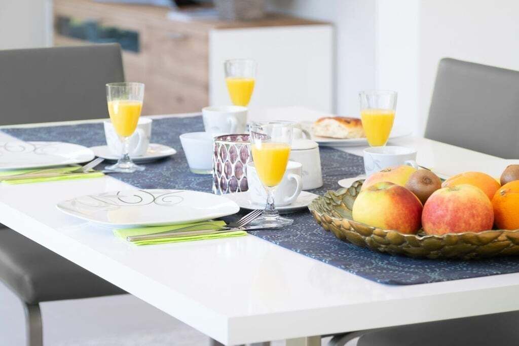 A breakfast table set with plates, glasses of orange juice, a pitcher, and a basket of fruit.
