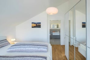 Ein modernes Schlafzimmer mit Bett, Nachttisch und Blick ins Badezimmer.