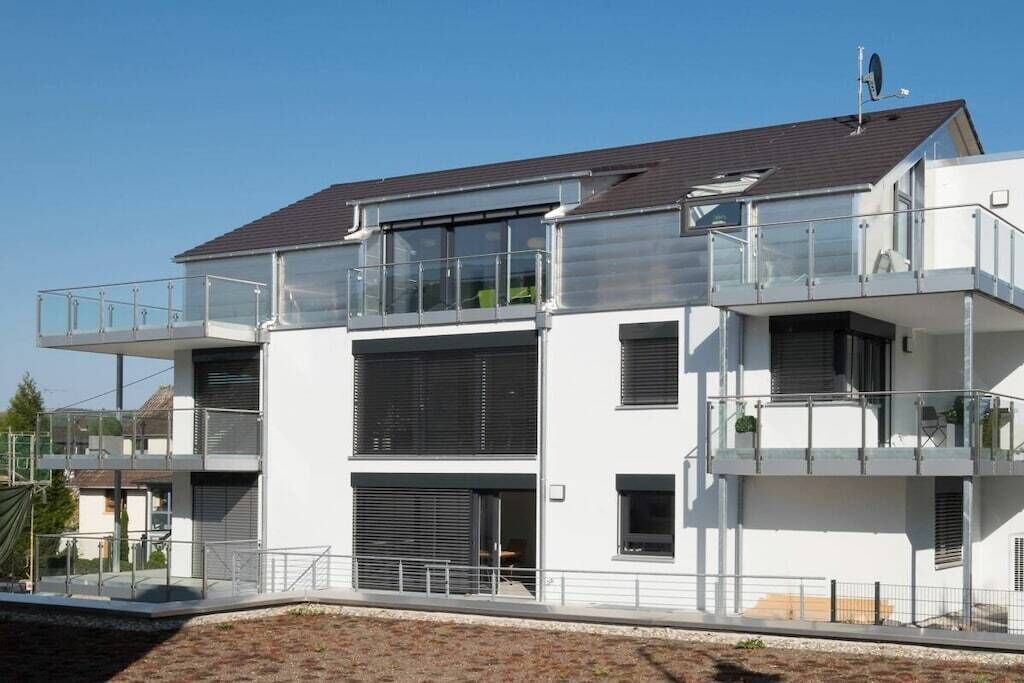 A modern multi-story residential building with balconies, large windows, and a flat roof.