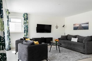 Un salon moderne avec un téléviseur à écran plat, deux canapés gris, une table basse ornée d’un vase et un tableau accroché au mur.