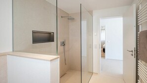 Un bagno moderno con box doccia in vetro, vaso sospeso e porta a vista che dà su un'altra stanza.