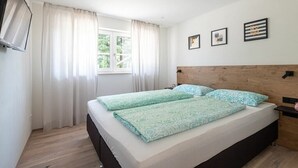 Una camera da letto con un letto, tende, una TV a muro e quadri appesi.