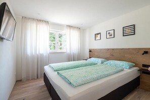 Ein Schlafzimmer mit einem Bett, Vorhängen, einem an der Wand befestigten Fernseher und gerahmten Bildern.