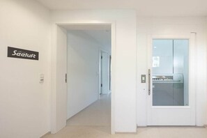 Un couloir avec une porte donnant sur une pièce séparée par une cloison en verre. Un panneau portant l’inscription « Seeluft » est visible sur le mur.