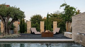 Area piscina con lettini, un braciere e un muro in pietra.