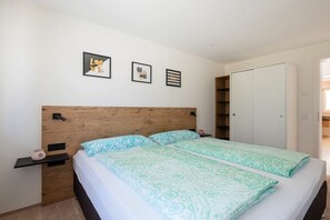 Une chambre à coucher avec une tête de lit en bois, deux lits avec une literie à motifs, une table de chevet, une armoire et des œuvres d’art murales.