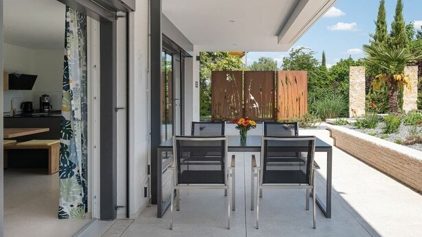 Zona pranzo all'aperto con tavolo e sedie, una recinzione in legno e vista sul giardino.